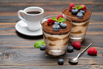 Classic tiramisu dessert with blueberries and strawberries in a glass cup and espresso coffee on wooden background