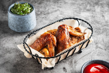 Chicken wings baked in a metal basket and seaweed, tomato sauce. Gray background, copy space.