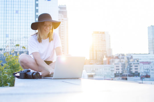 girl photographer sitting with camera and laptop outdoors and retouching photo, tourist freelancer on a background of city sunset