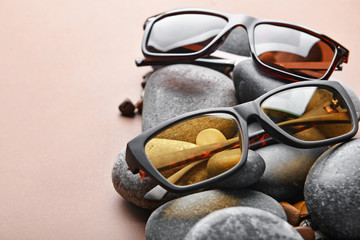 Stylish sunglasses and pebbles on color background