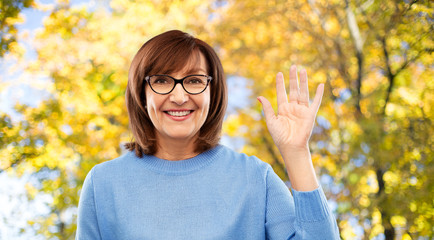 gesture, vision and old people concept - portrait of smiling senior woman in glasses waving hand over autumn park background © Syda Productions