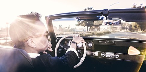 Young man driving vintage convertible down empty backlit road