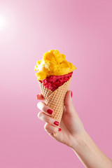 Woman hand holding ice cream cone on a pink background. Copy space