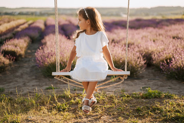 Little Girl on Swing Lavender Field Background. Pretty Kid in White Dress Sitting on Flip Flap....
