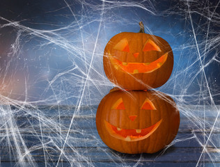 holidays, halloween and decoration concept - two pumpkins or jack o lanterns on table and spiderweb...