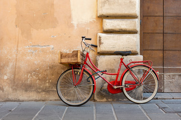 Fototapeta na wymiar Red classic model women's bicycle with a lock parked against the wall in the Italian city of Foligno.