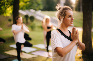 Obraz premium Young woman is meditating standing up in park while sunrise Group of people meditating background. Hand in Om position. Girls are meditating at dawn
