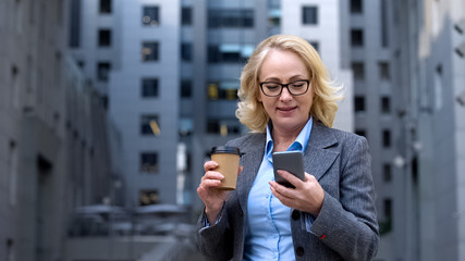 Active modern business woman reading smartphone email holding coffee cup outdoor