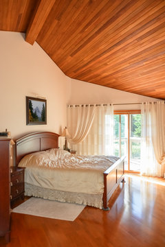 Beautiful bedroom with wooden ceiling and sun light coming through glass door.