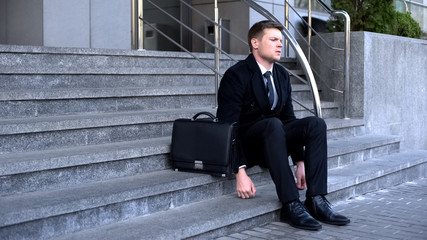 Depressed young man sitting office stairs, job interview failure, unemployment