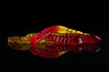 Group of three whole crimson yellow colourful jelly worm candy isolated on black glass
