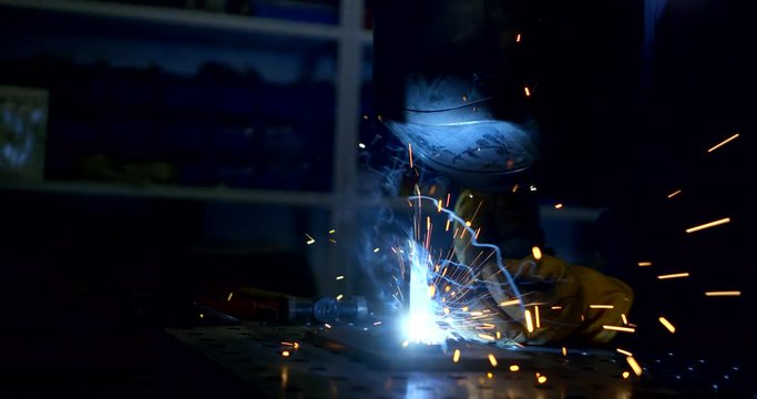worker welds details using modern tool with sparkles in room