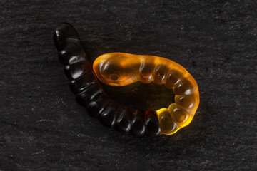One whole orange brown colourful jelly worm candy flatlay on grey stone