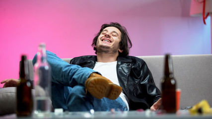Relaxed drunk young man sitting on sofa, boozer enjoying music at dance party