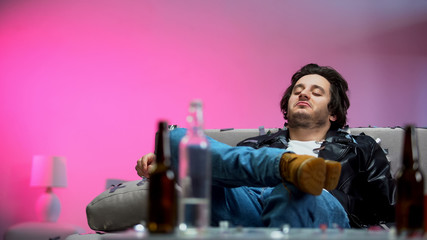 Pleased man sitting on sofa, enjoying home party, alcohol addiction, confetti