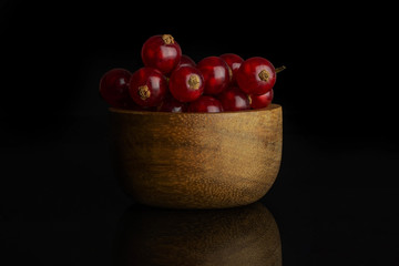 Lot of whole fresh red currant in bamboo bowl isolated on black glass