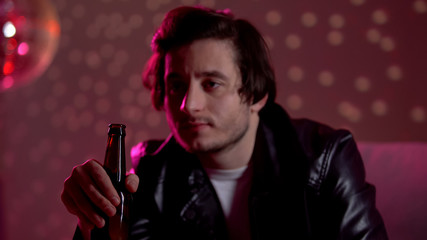 Young guy with beer bottle thinking about difficult life in night club, relax