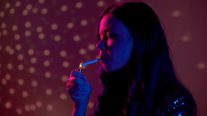 Fototapeta premium Woman lighting cigarette in night club, harmful addiction, lungs cancer risk