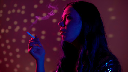 Serious young woman smoking cigarette at nightclub party, unhealthy habit