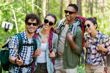 travel, tourism, hike and people concept - group of friends with backpacks taking selfie by smartphone in forest