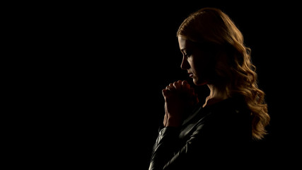 Blond woman praying in dark place, asking for forgiveness, sinner confession
