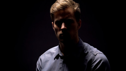 Shy shadowed man looking at camera on black background, mens health, criminal