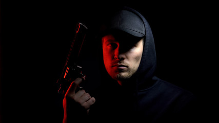 Male hooligan with gun against dark background, danger criminal ready to robbery