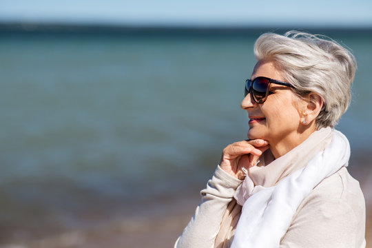 people and leisure concept - portrait of happy senior woman in sunglasses and scarf on beach in estonia