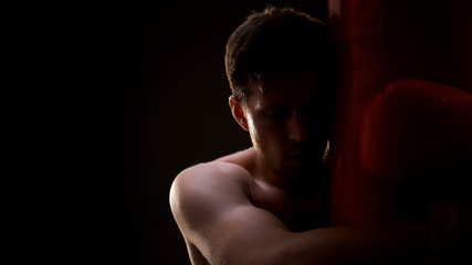 Fototapeta premium Exhausted sportsman holding boxing bag, failed in fight with problems, concept