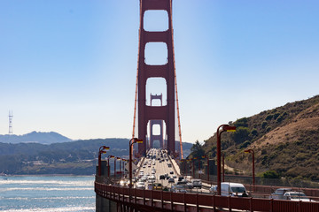 Two way midday traffic and people/ tourists/ pedestrians walking on the iconic Golden Gate Bridge...