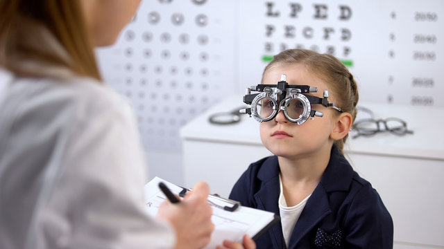 Cute girl in optical trial frame waiting prescription from ophthalmologist