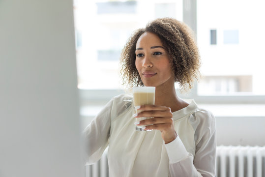 Young businesswoman with Latte Macchiato looking at computer