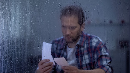 Sad middle-aged man putting together two parts of torn photo, missing wife