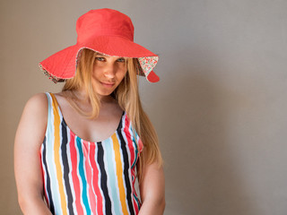 Slender charming young blonde in a colorful swimsuit and pink hat poses in front of the camera in the studio