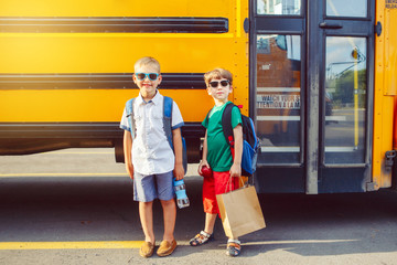 Two funny happy Caucasian boys students kids with apples in sunglasses near yellow bus on 1...
