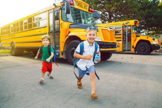 Two funny happy Caucasian boys students kids running near yellow bus on 1 September day. Education and back to school concept. Children friends pupils ready to learn and study.