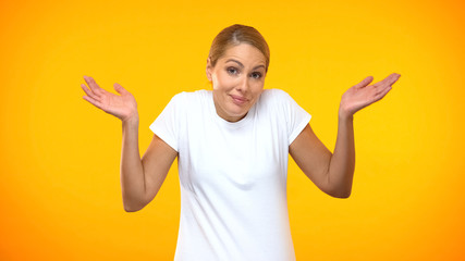 Doubtful woman throwing up hands on bright background, having no idea, choice