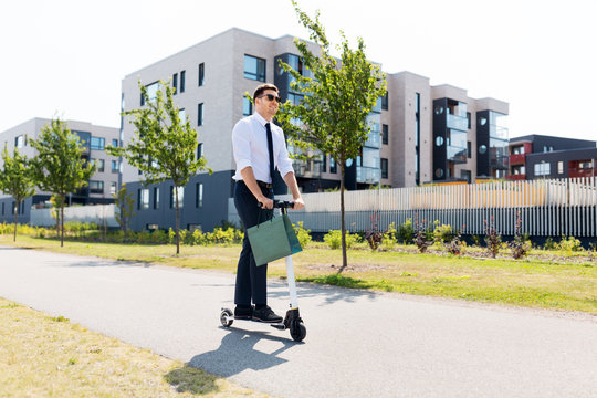 business and people and concept - young businessman with shopping bag riding electric scooter outdoors