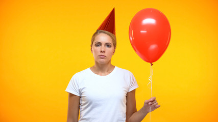 Upset female with red balloon in hand, feeling lonely on birthday party, sadness