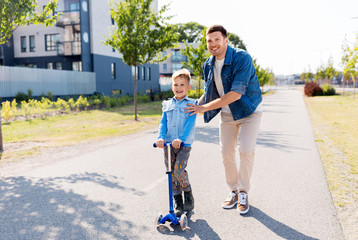 Fototapeta premium family, leisure and fatherhood concept - happy father spending time with little son riding scooter in city