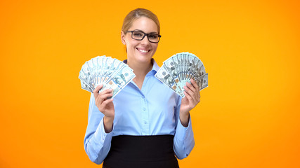 Smiling business lady showing dollar bills on orange background, investment