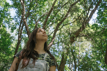 A young woman in casual clothes is smiling and looking at the top in the park.