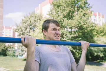 A young handsome man in casual clothes is doing pull up exercise on horizontal bar. fitness, sport, exercising, training and lifestyle concept - young man doing pull ups on horizontal bar outdoors