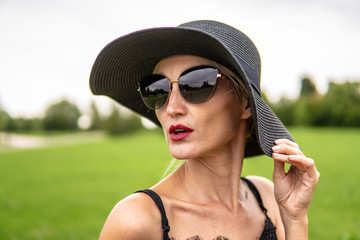 Fototapeta premium The girl loves on the field in photochromic glasses in a black hat from behind a beautiful forest.