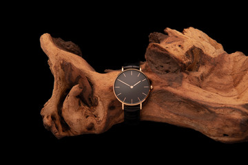 A black watch with a gold case hung on a piece of wood wellington