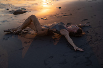 Beautiful sensual woman in sparkling swimsuit posing at the black sand beach during amazing golden sunset