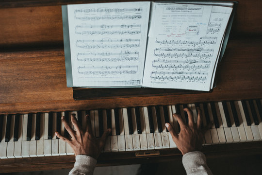 A piano showing a mans hands, the keys and sheet music.