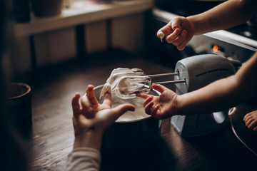 Several small hands fingering whip cream off of the mixer blades.