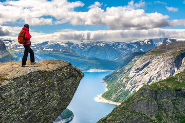 Naklejka premium Kobieta turysta stoi na skale i patrzy na widok z lotu ptaka w górach. Niesamowity widok przyrody w drodze do Trolltunga. Lokalizacja: Góry Skandynawskie, Norwegia, Stavanger. Poczucie całkowitej wolności