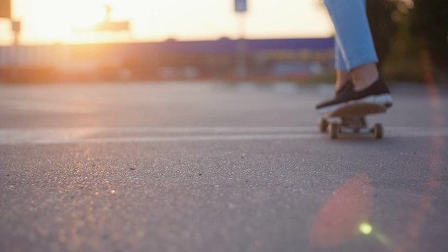 Young girl riding on the skateboard on the asphalt road on the parking at sunset. Legs of skateboarder in slow motion